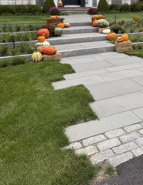The front walk of the house in autumn: bluestone paving and granite steps edged with cobbles, with pumpkins and mums along the steps.