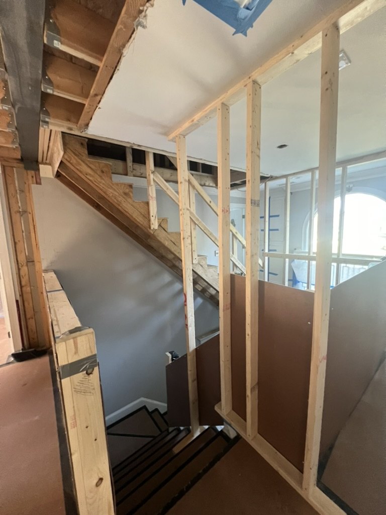 A staircase mid-renovation: bare stud framing, exposed joists and a stair stringer open to the floor below.